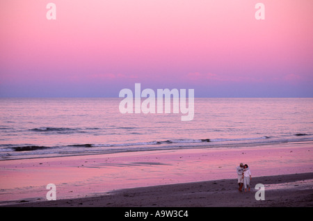Romantic couple young man and woman walking along sand of Duxbury Beach at sunset dusk in Massachusetts, New England, USA Stock Photo