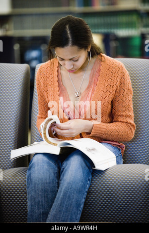 Young woman reading a book sitting on the sofa in library Stock Photo