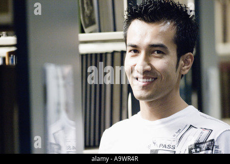 Portrait of a smiling young man amidst library book stacks Stock Photo