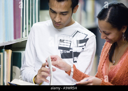 Students reading a book amidst library book stacks Stock Photo