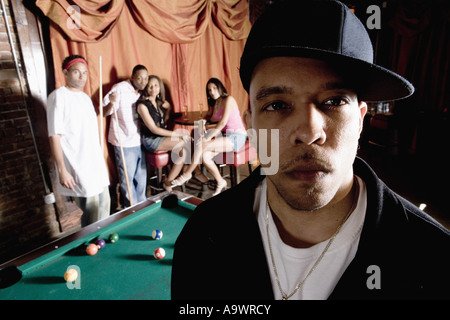 Close-up of a young man in hip-hop fashion with people shooting pool in background Stock Photo