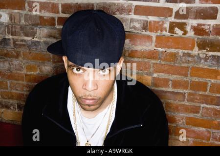 Portrait of a young man in hip-hop fashion sitting against brick wall Stock Photo