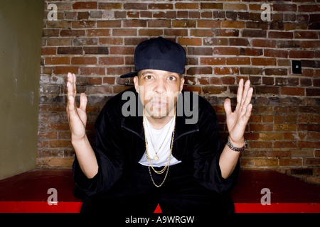 Portrait of a young man in hip-hop fashion sitting against brick wall Stock Photo