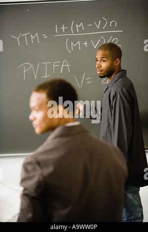 Student writing on the chalkboard in front of teacher Stock Photo