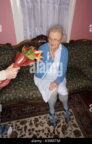Surprised and happy senior woman sitting on the sofa handed bouquet of flowers Stock Photo