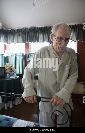 Feeble senior man trying to walk while holding on to bedframe Stock Photo