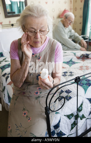Senior woman sitting on bed looking at prescription bottle