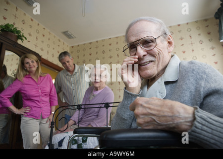 Elderly man whispering to camera with spouse and adult children in background Stock Photo