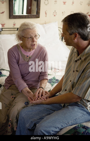 Senior woman with adult son conversing while sitting on bed Stock Photo