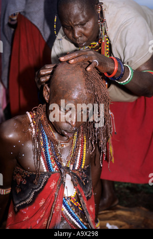 Lolgorian, Kenya. Siria Maasai; Eunoto ceremony; moran having his braided hair shaved off by a woman. Stock Photo