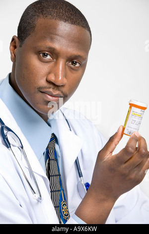 Young serious looking doctor wearing a white coat holding a jar of pills Stock Photo