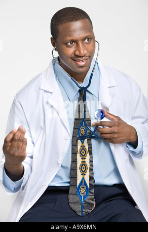 Young doctor listens to his own heart, perhaps to relax a patient who is feeling tense. He's wearing a white coat and smiling. Stock Photo