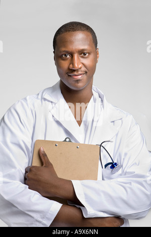 Young black doctor wearing a white coat and stethoscope holding a clipboard and smiling at the camera Stock Photo