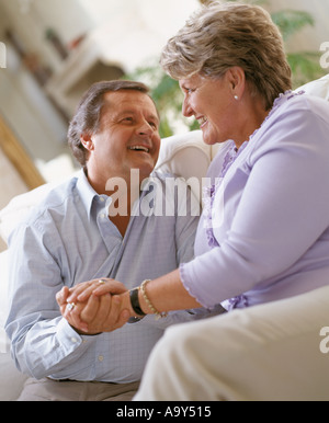 middle aged couple laughing and holding hands on sofa Stock Photo
