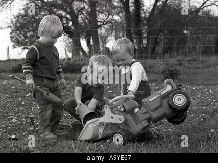 Retro image of three young boys playing out together outside in a garden with a toy digger bucket and spade England UK Britain Stock Photo