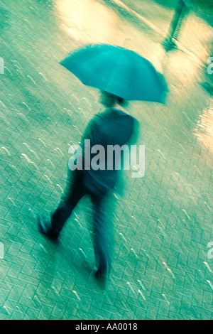 Business man walking over cobbled ground with umbrella in a suit during a downpour of rain in the city of Chester, Cheshire, England, UK Stock Photo