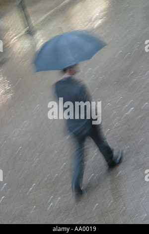 Business man walking over cobbled ground with umbrella in a suit during a downpour of rain in the city of Chester, Cheshire, England, UK Stock Photo