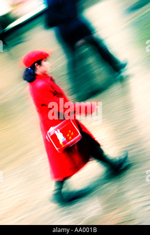 A woman walking in red coat and hat fast across cobbled ground during rain, blurred due to speed, Chester, Cheshire, UK
