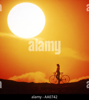woman pauses beside bicycle to watch huge sunset Stock Photo