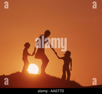 mother walking on hill with small son and daughter at sunset Stock Photo
