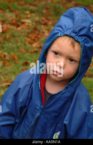 Little boy wearing a blue waterproof raincoat looking concerned Stock Photo