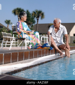 Retired couple sitting by a swimming pool in a tropical climate Stock Photo