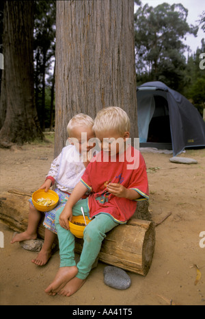 Little boys, two and four years old, are sitting on a log for eating muesli, campground in South Africa Stock Photo