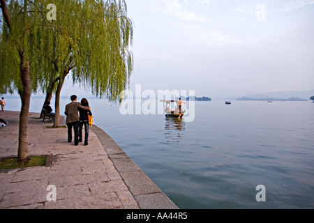 CHINA HANGZHOU Chinese couple walking under willow trees on the shore of West Lake in Hangzhou China at sunset Stock Photo