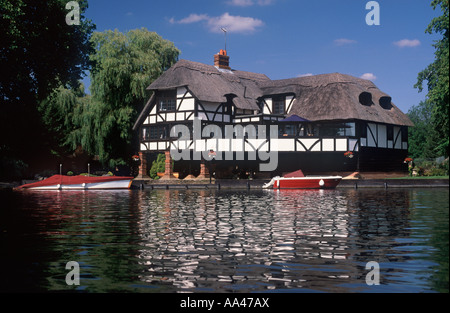 Thatched timber framed mansion on River Thames with moored slipper launch and motor cruiser, near Henley on Thames, England Stock Photo