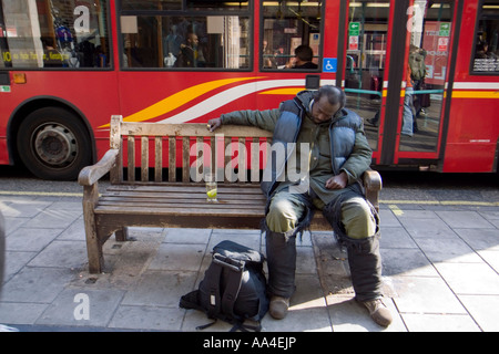 Homeless man falling asleep on a bench with a glass of gin tonic on his side, Oxford street, London ,UK Stock Photo