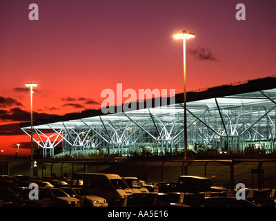 London Stansted Airport in Essex main terminal building landscape glass facade front car rental car parks in foreground winter sunset sky England UK Stock Photo