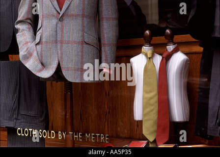 Savile Row tailor shop window with miniature judies and ties, wool jacket, pin striped trousers & sign: Cloth Sold By The Metre Stock Photo