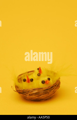 Cute Easter chick toy novelties in a small wicker basket against a bright vivid yellow Easter background Stock Photo