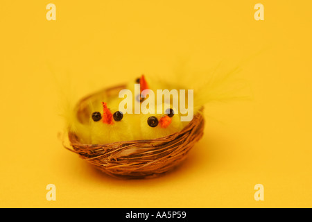 Cute Easter chick toy novelties in a small wicker basket against a bright vivid yellow background room for text Stock Photo
