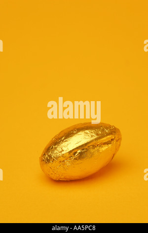 One 1 single bright coloured golden Easter egg in foil wrapper chocolate confectionary with a seasonal Spring yellow background Stock Photo