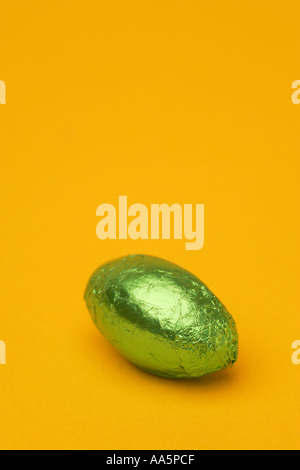One 1 single bright coloured green Easter egg in foil wrapper chocolate confectionary with a seasonal Spring yellow background Stock Photo