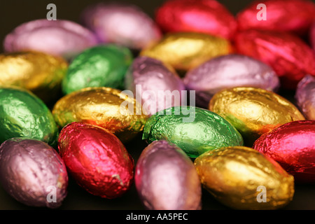 Colourful bright foil wrapped mini chocolate seasonal Spring Easter eggs candy sweets confectionary striking black background Stock Photo