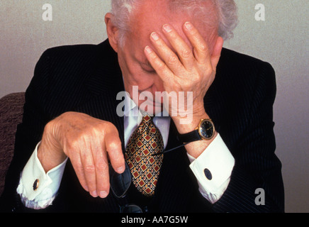 elderly tired discouraged formally well dressed businessman alone in office with his hand to his head Stock Photo