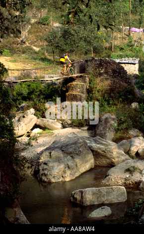 Mountain biker crosses rickety suspension bridge over river gorge in Nepal mountains Stock Photo