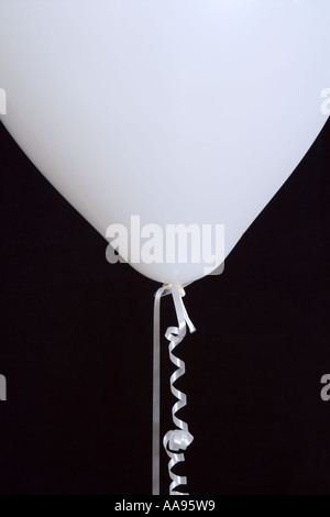 White balloon and curled ribbon against black background, close-up Stock Photo