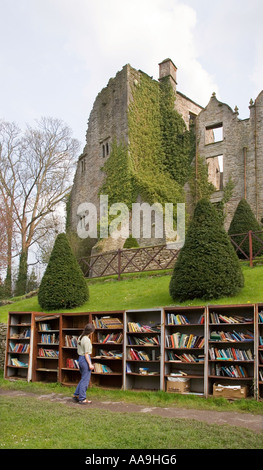 Woman looking at used books for sale on outdoor shelving in front of ruined castle Hay on Wye Wales UK Stock Photo