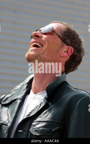 man in his forties wearing a green leather jacket and sunglasses laughs out loud Stock Photo