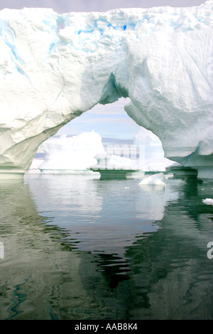 dramatic ice arch is reflected in the calm sea at Pleneau icegarden Antarctica Stock Photo