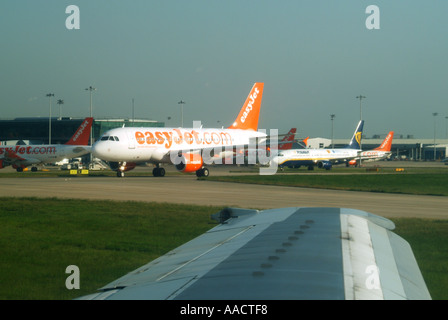 View from inside passenger jet aircraft about to take off showing wing tip and various other planes on ground Stock Photo