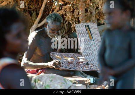 Johnny Bungawuy paints sugar bag dreaming with natural ochres on bark in a bough shade Nangalala Arnhem Land Australia Stock Photo