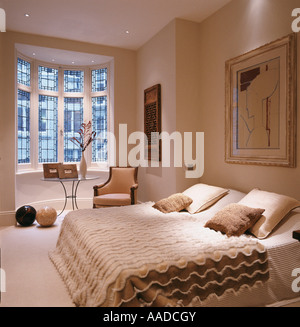 Double bed with textured cover in cream bedroom with artwork and window Stock Photo