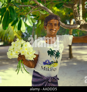 Young smiling Maldivan man in white t-shirt holding bunch of Frangipani flowers on an Bandos island in The Maldive Islands Stock Photo