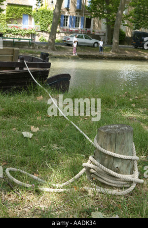 rope tied to mooring post on side of canal with the boat and local residents in the distance Stock Photo