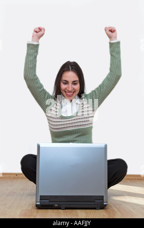 Young woman sitting on floor using laptop arms raised Stock Photo