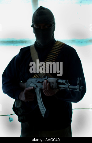 a terrorist dressed in a balaclava holding an AK47 kalashnikov rifle and wearing a belt of bullets next to a land rover posed by model Stock Photo